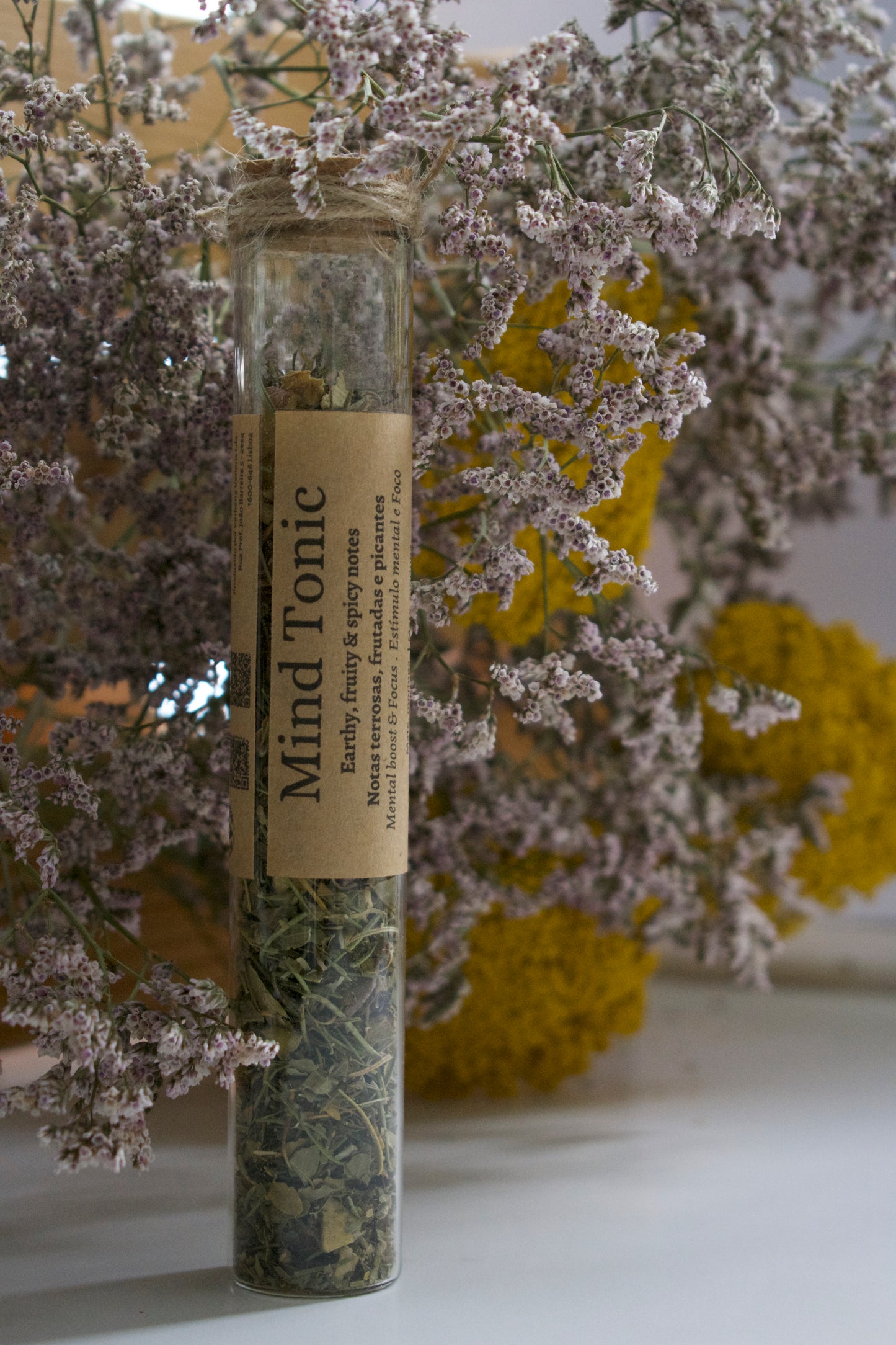 Glass tube Mind Tonic, loose leaves tea, standing up with a floral background.