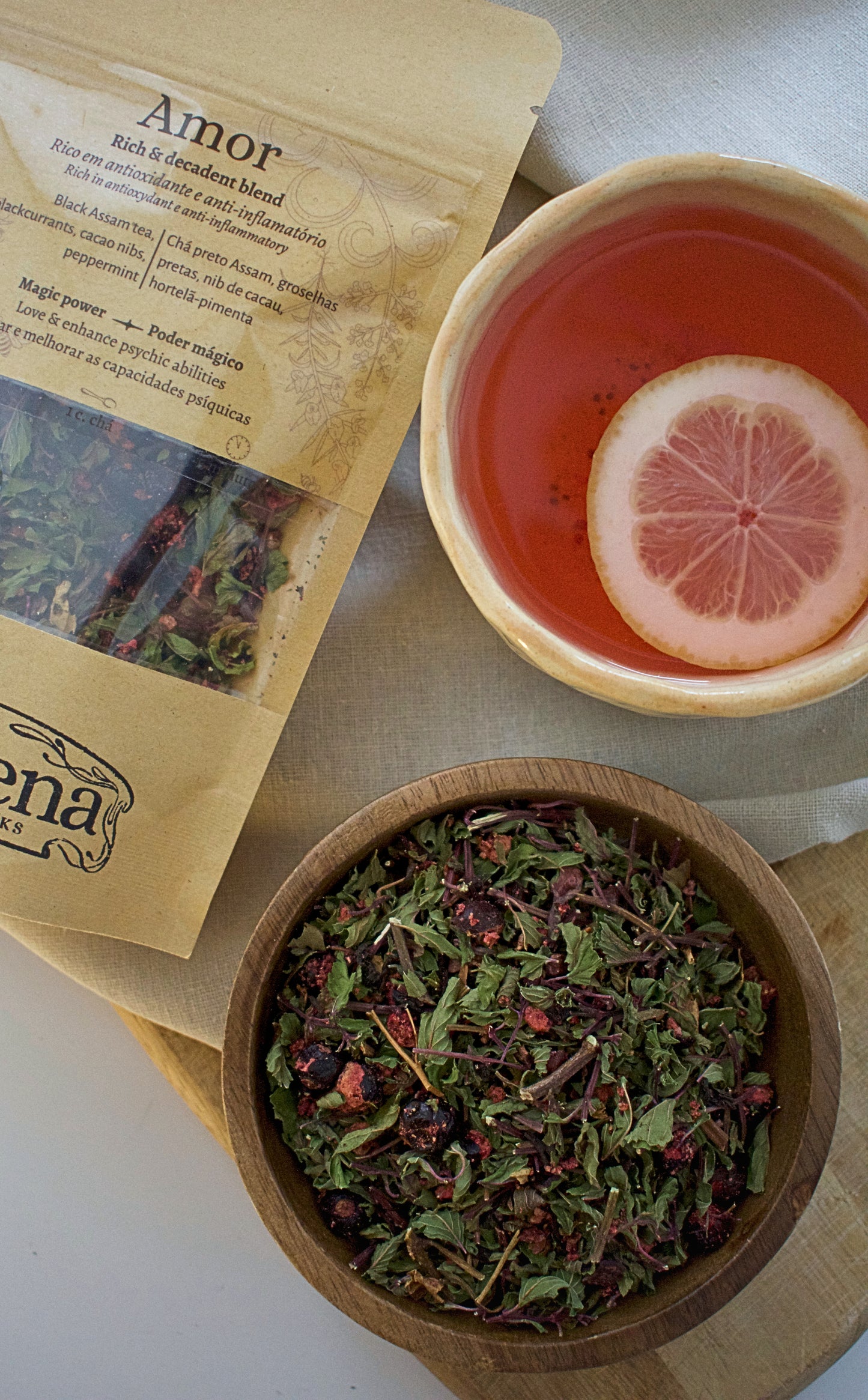 Tea packaging, bowl of tea leaves, and cup of tea with a slice of lemon on a light surface.