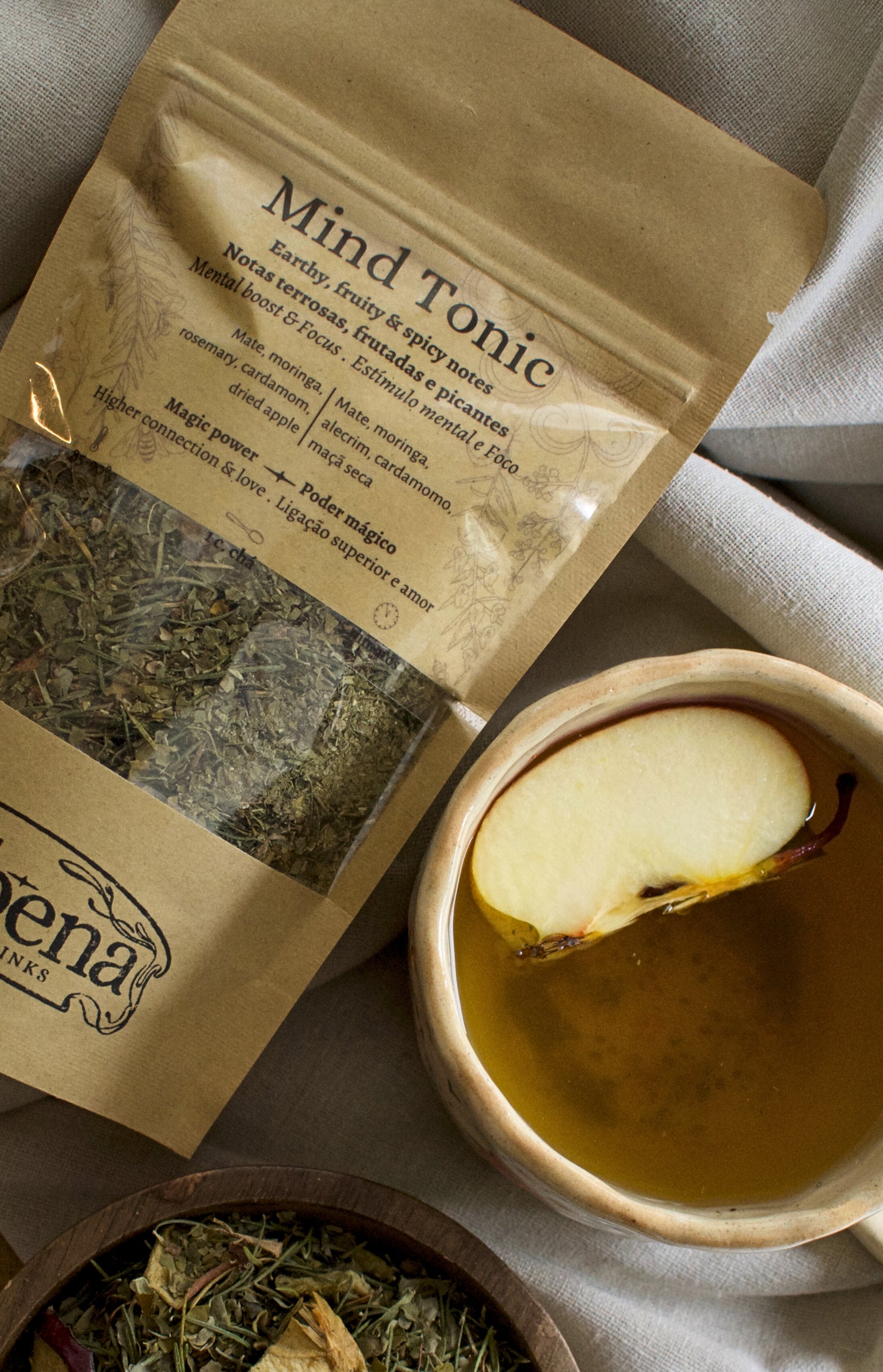 Tea bag 'Mind Tonic' with a cup of tea and dried herbs on a linen cloth