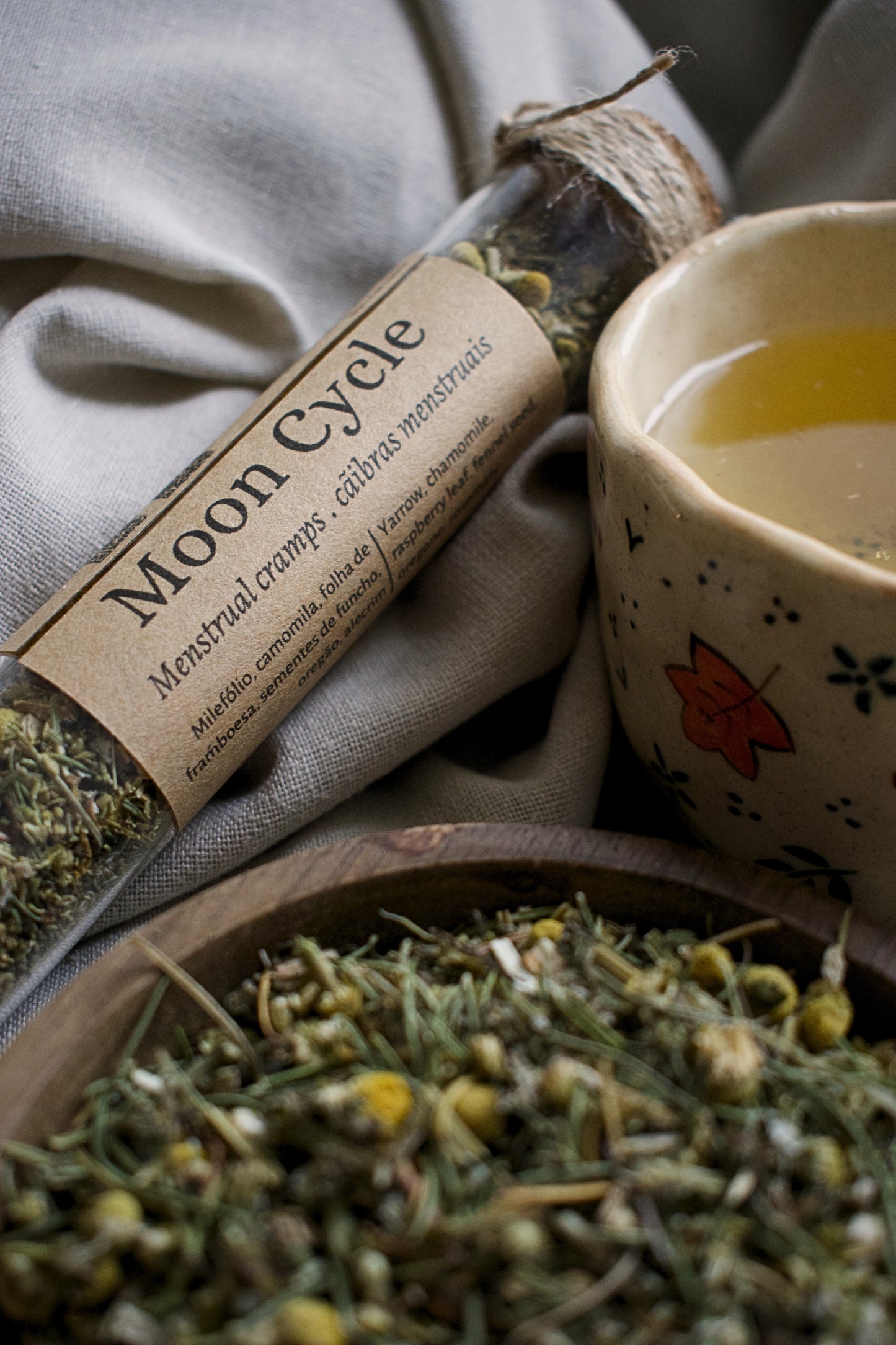 Herbal products including a roll labeled 'Moon Cycle' and a small cup with a floral design on a textured surface.