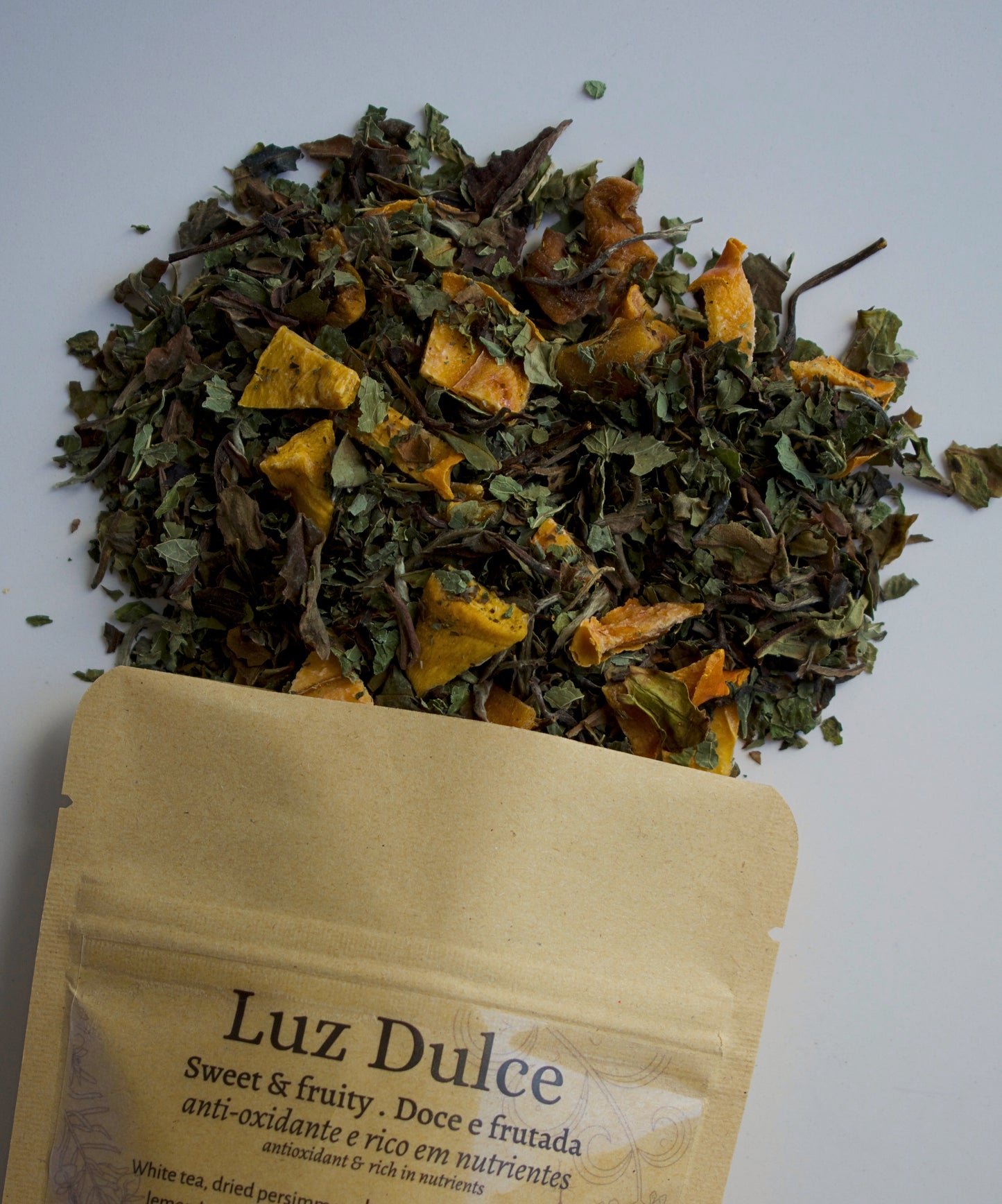 Luz dulce tea blend spilled on a white background, coming out of a kraft bag with a transparent label with "Luz Dulce" on it.