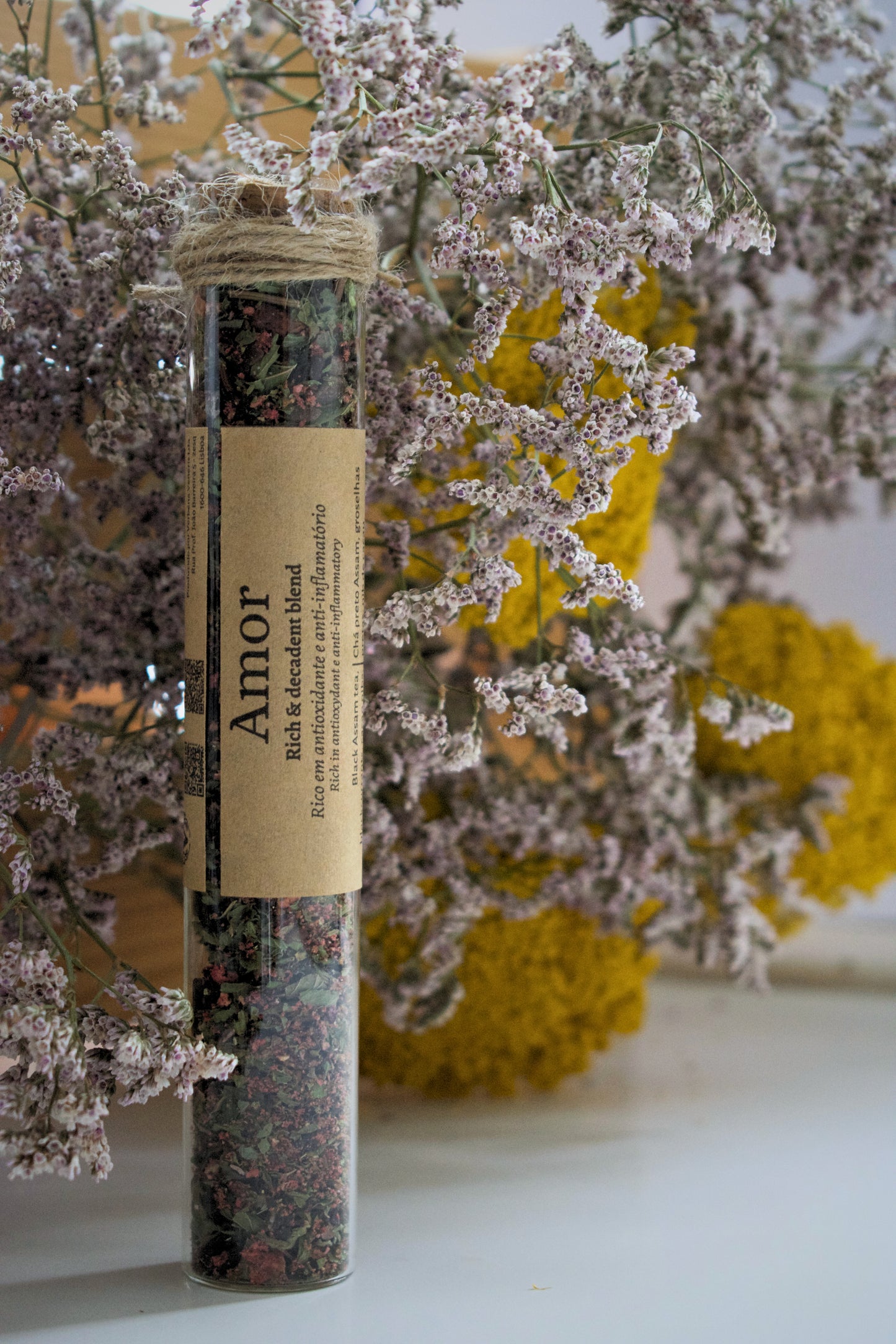 Amor tea blend in a glass tube on a floral background.