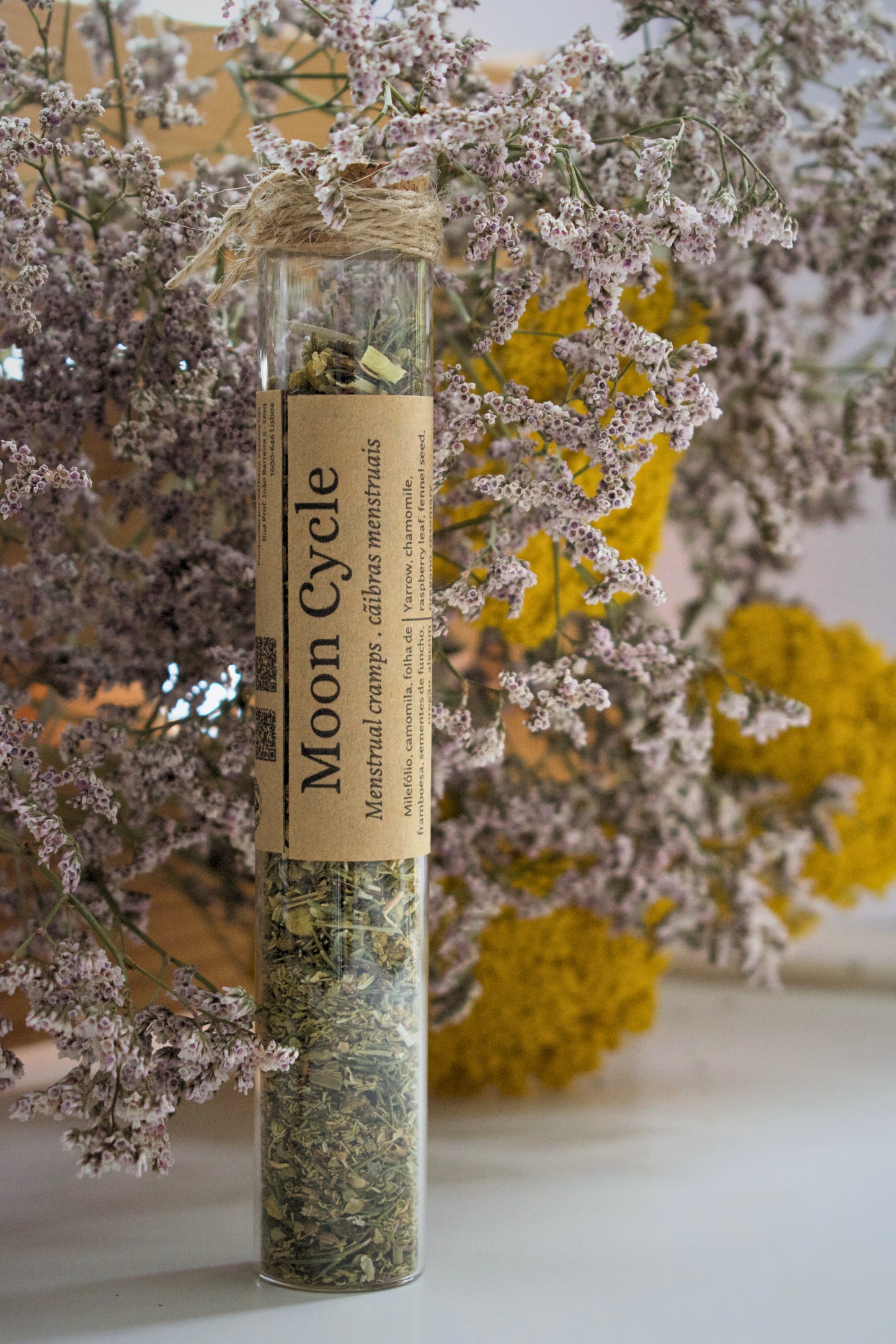 Herbal product in a glass tube labeled 'Moon Cycle' with flowers in the background