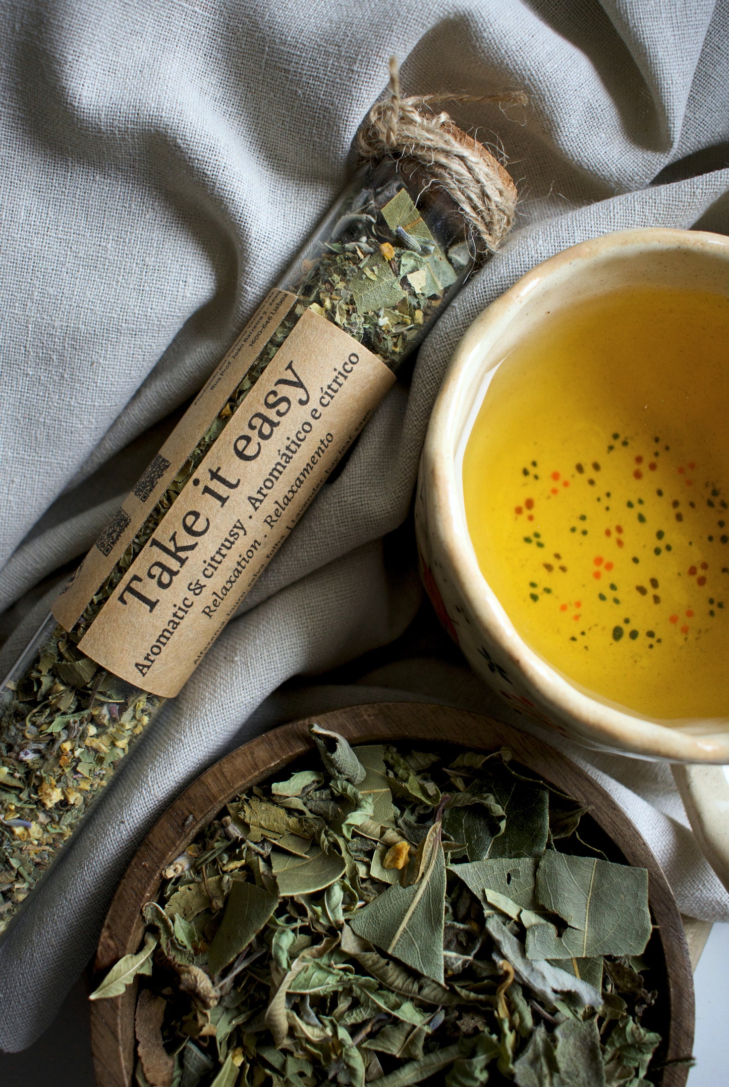 Glass tube with a labeled 'Take It Easy' next to a bowl of yellow liquid and a wooden bowl of dried herbs.