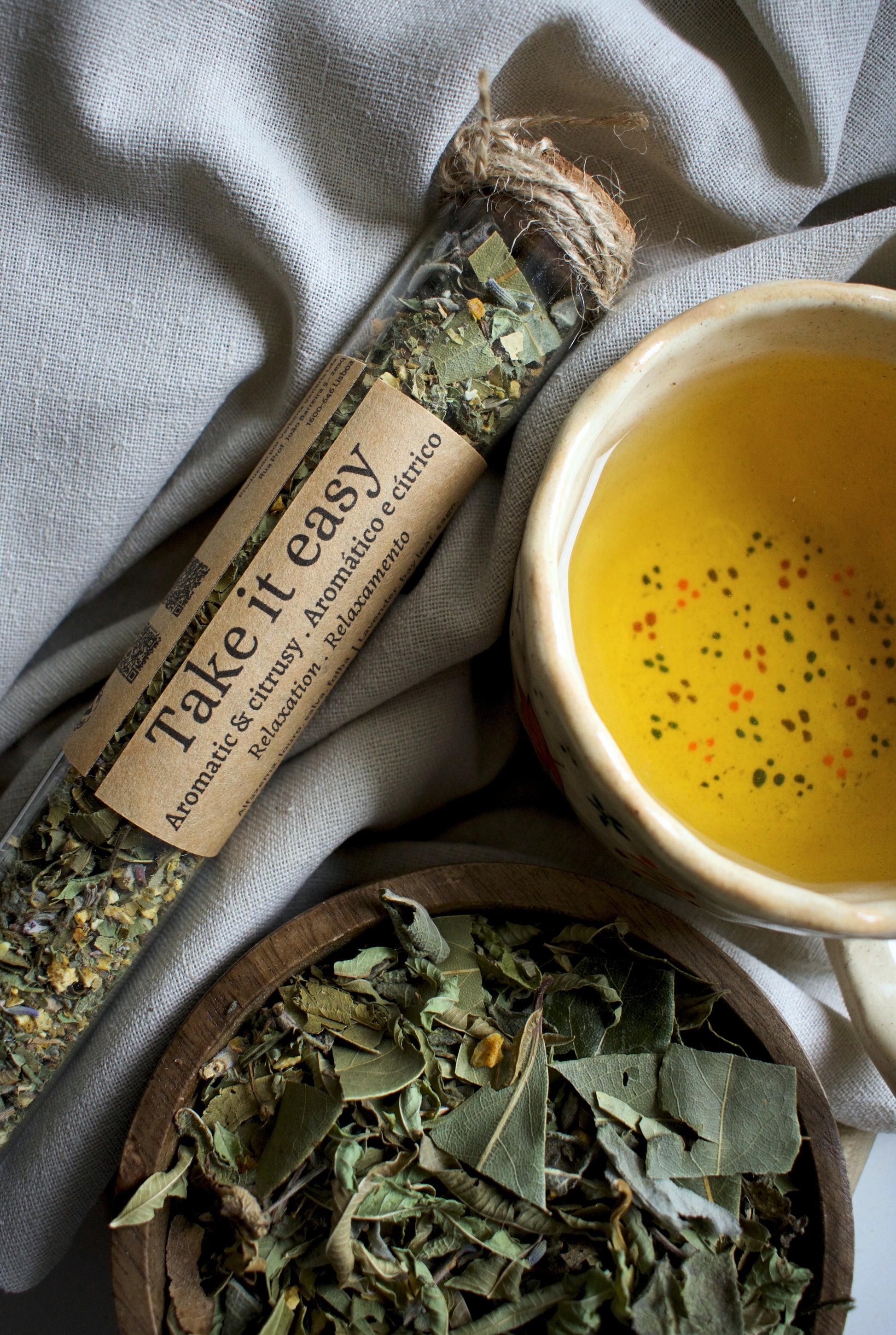 Glass tube with a labeled 'Take It Easy' next to a bowl of yellow liquid and a wooden bowl of dried herbs.