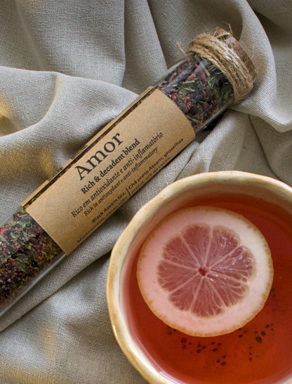 Amor tea blend in a glass tubes, next to a tea cup with a slice of lemon on a linen cloth.