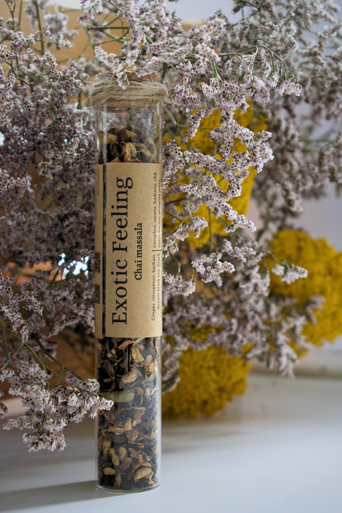 Glass tube with dried herbs labeled 'Exotic Feeling' against a floral background