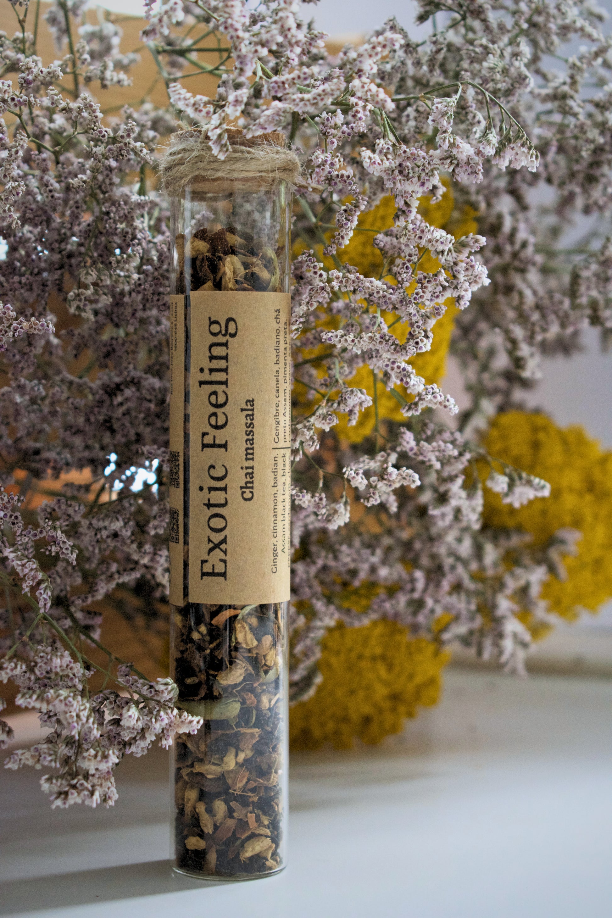 Glass tube with dried herbs labeled 'Exotic Feeling' against a floral background